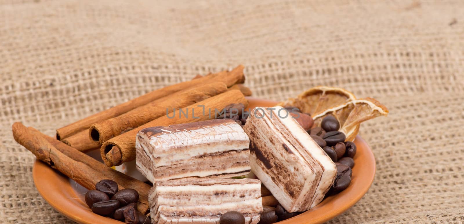 Sweets, cinnamon, nuts and coffee beans on a saucer, on burlap background.