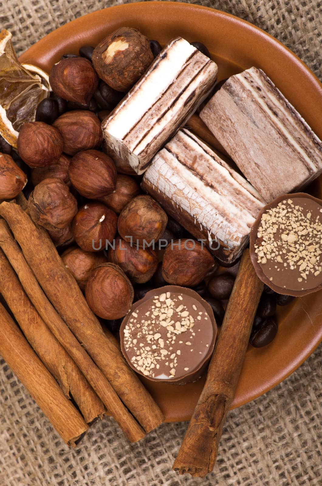 Sweets, cinnamon, nuts and coffee beans on a saucer, on burlap background.