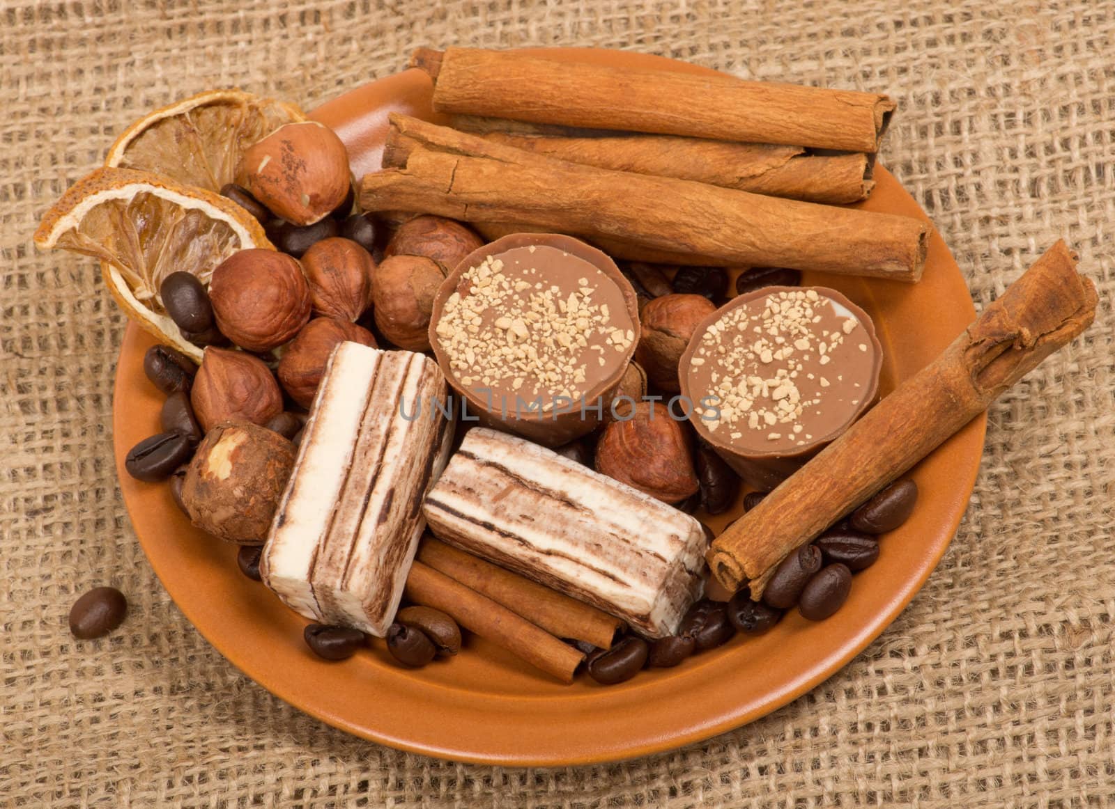 Sweets, cinnamon, nuts and coffee beans on a saucer, on burlap background.
