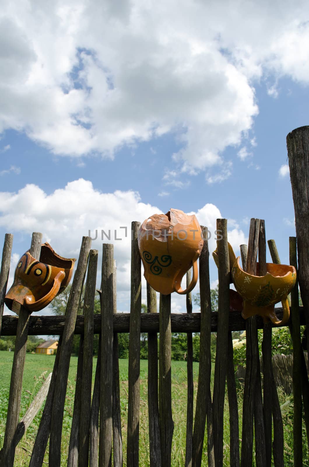 several clay broken pitchers hang on retro wooden fence from woven tree branches.