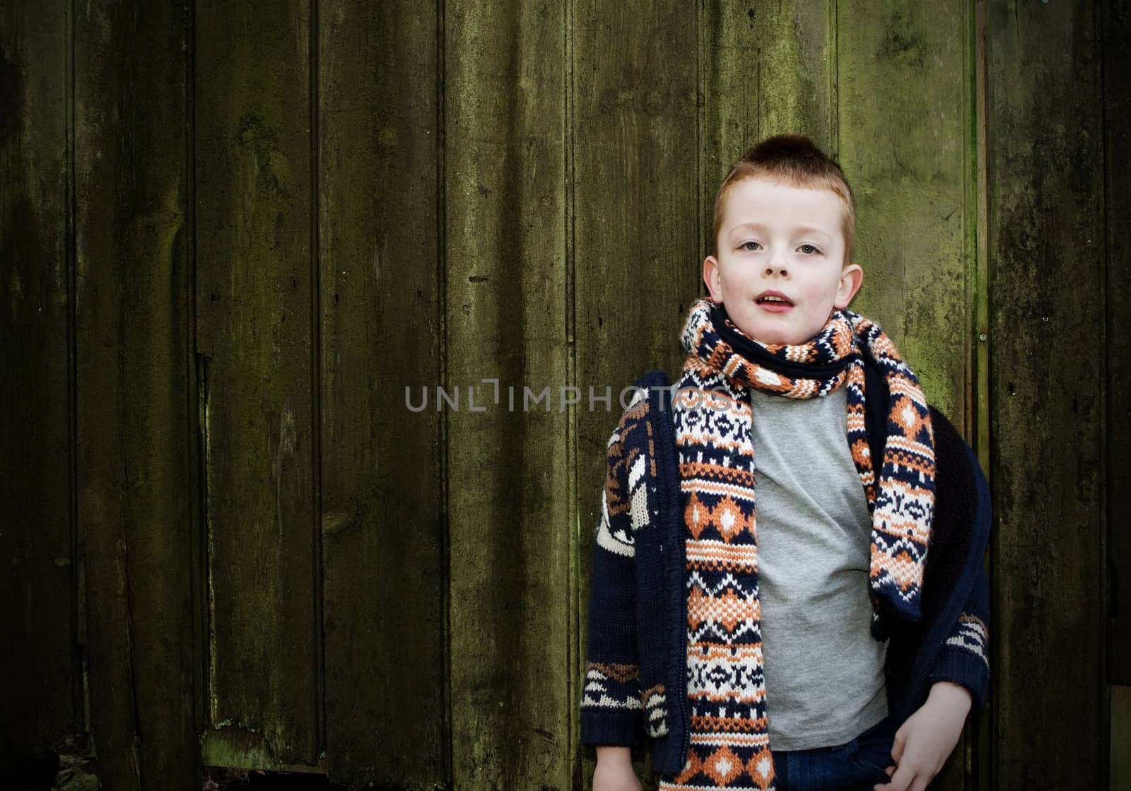 little boy standing against a wooden background