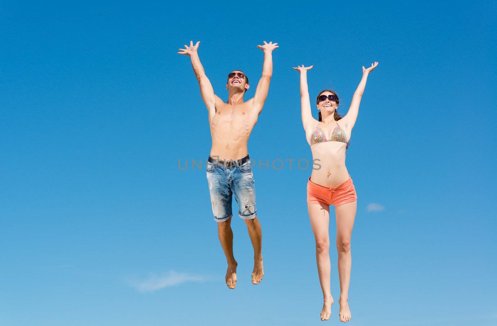 young couple jumping together on a blue sky background