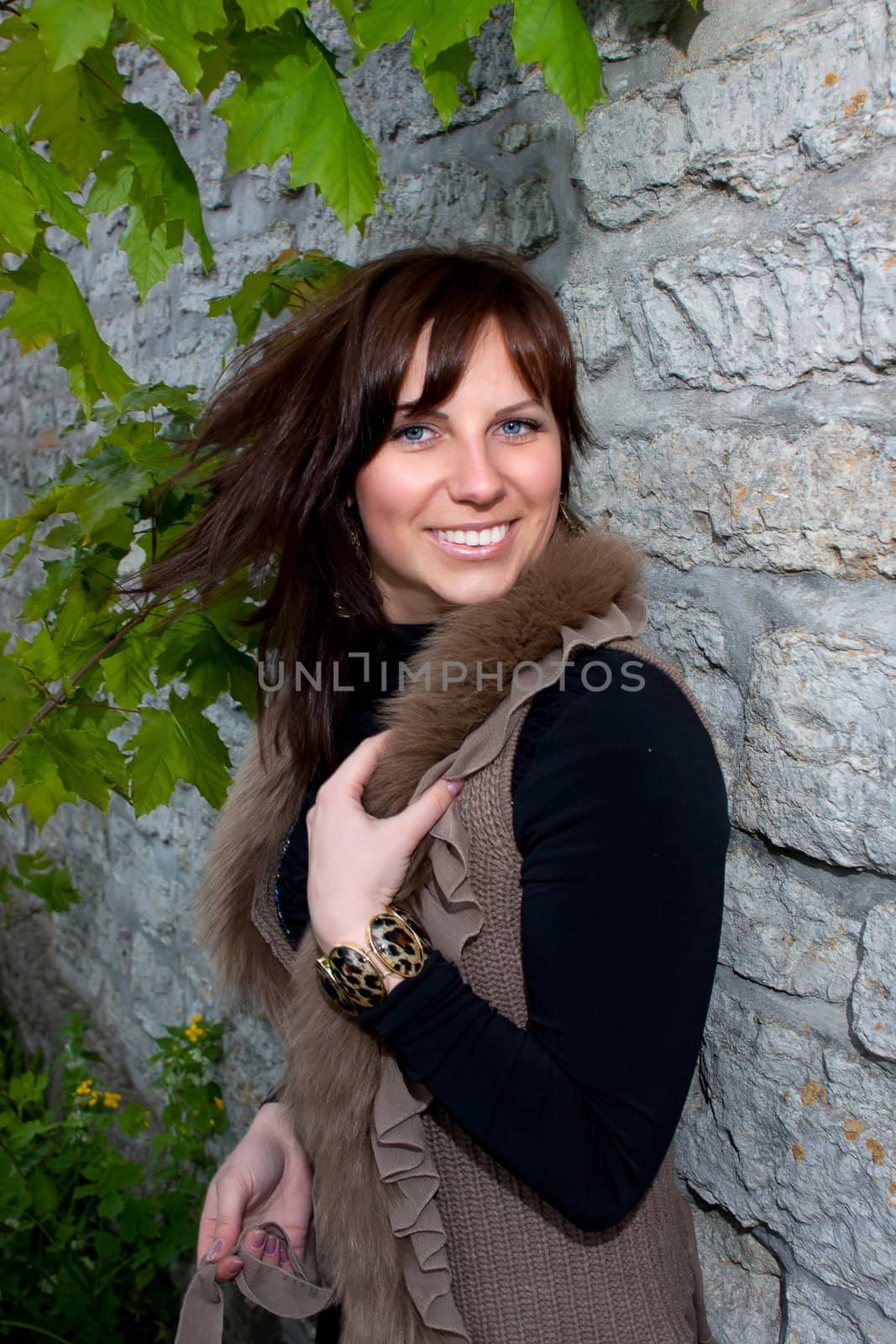 Beautiful blue-eyed smiling girl outdoors near the wall and maple