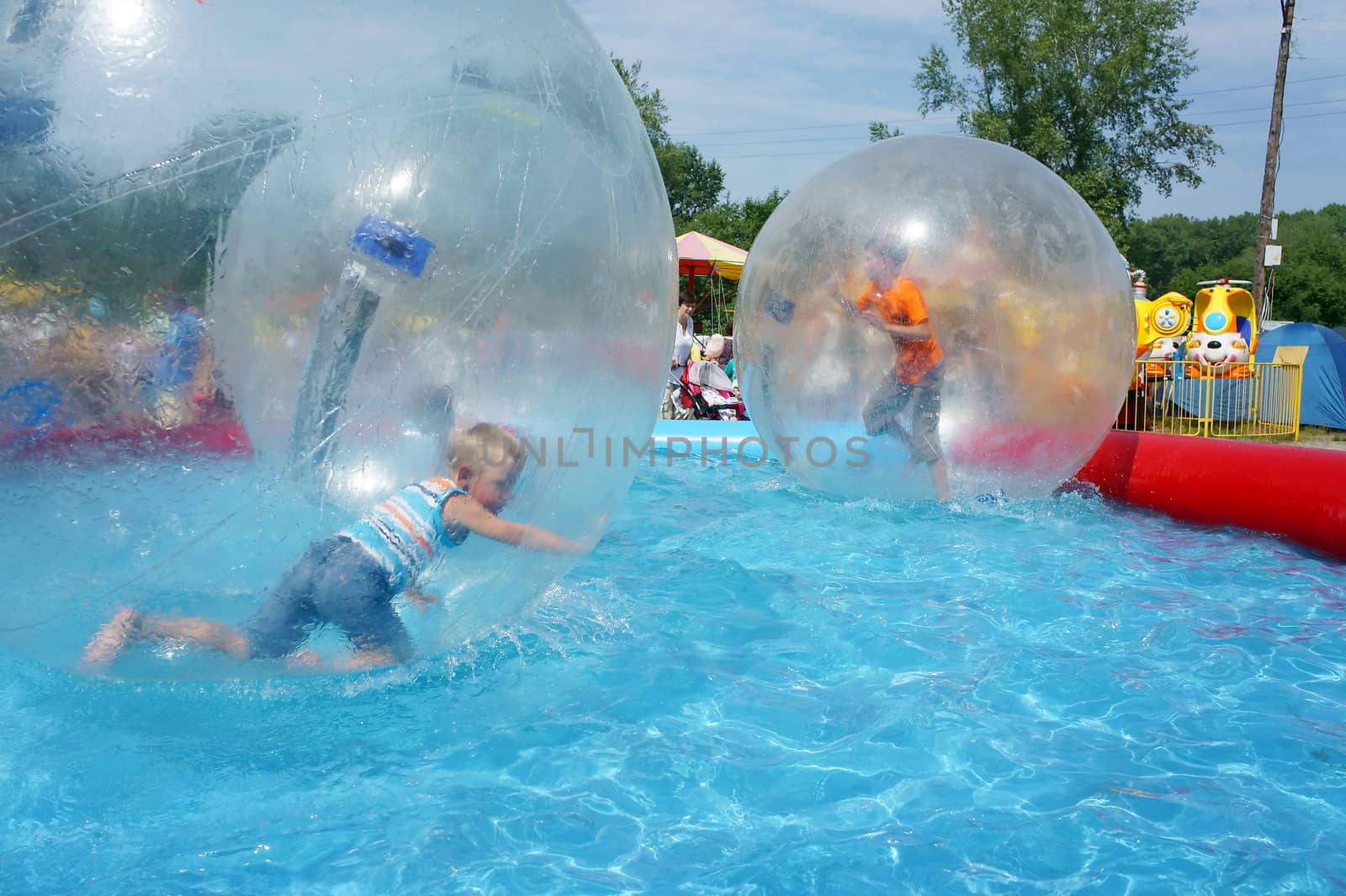 Boys riding in a large zorb balls in the pool on a summer day.