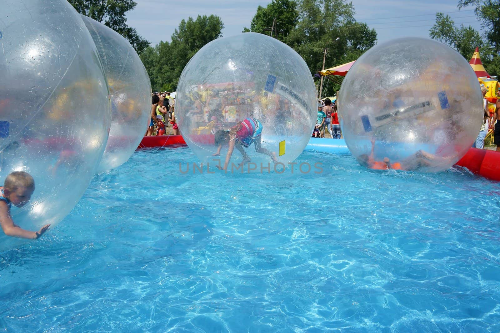 Children riding in a large zorb balls in the pool on a summer day.