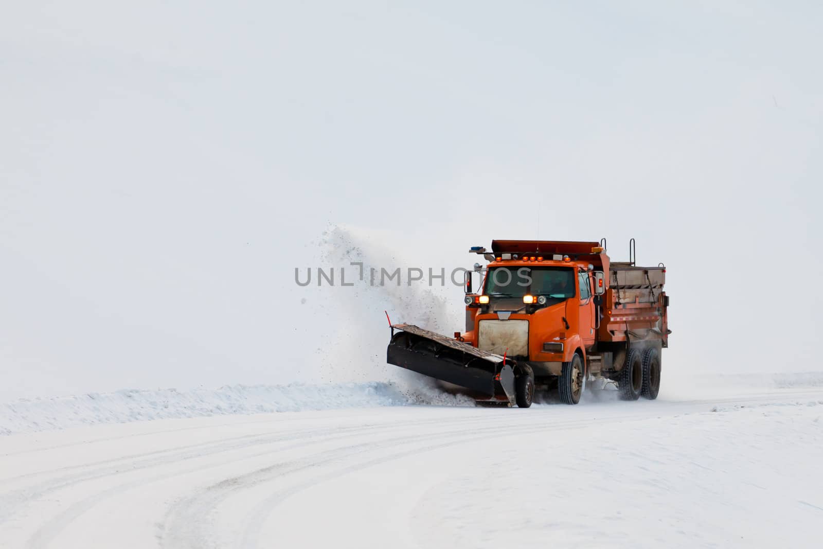 Snow plough truck clearing road after whiteout winter snowstorm blizzard for vehicle access