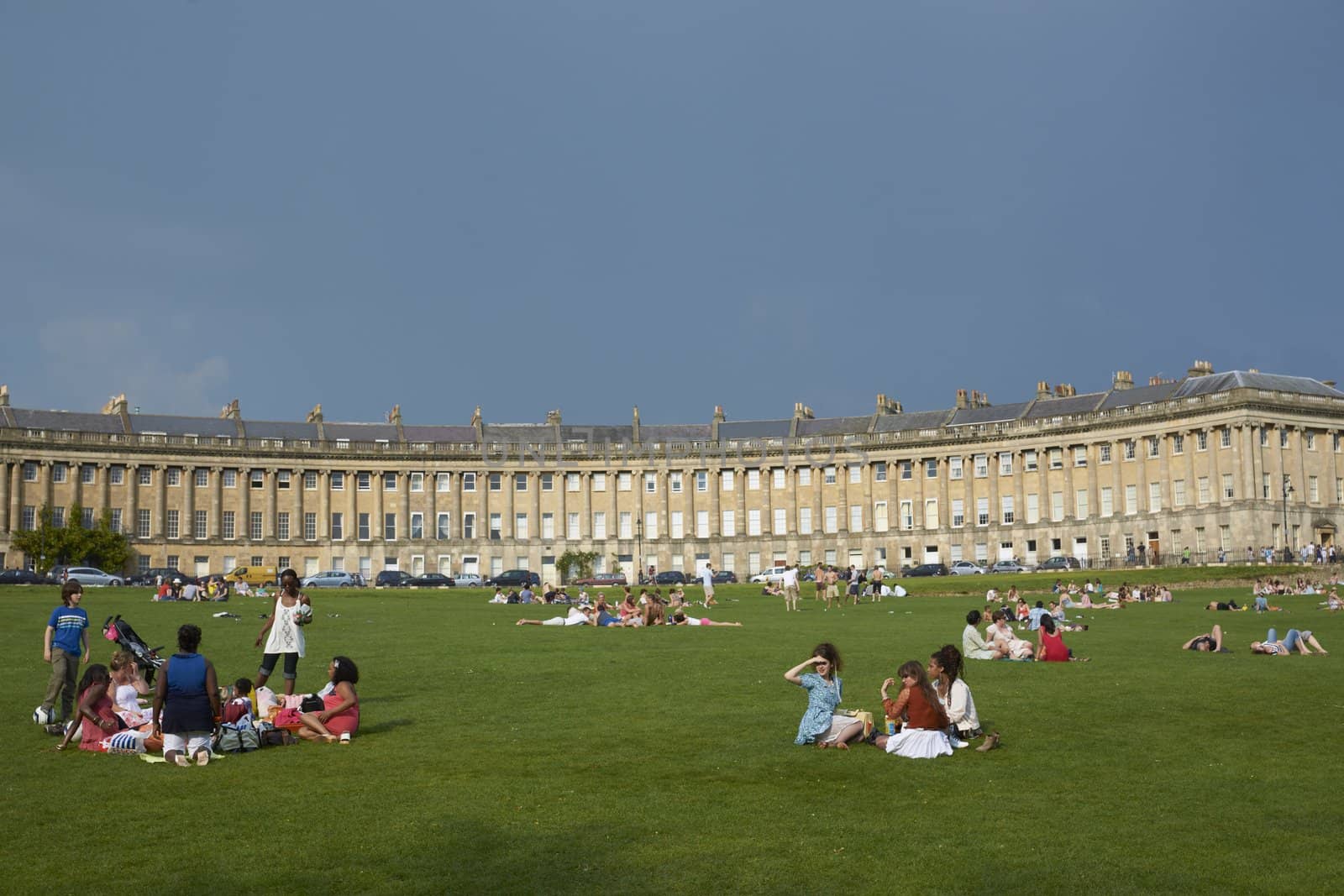 Groups of people enjoying the sunshine on the grass in front of the Royal Crescent in Bath, Somerset, England.
