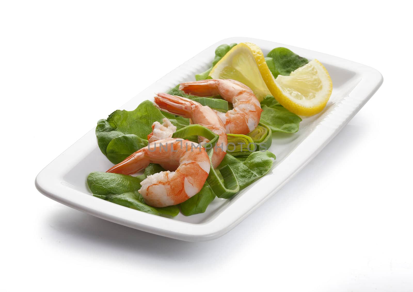 Three shrimp's tails with leek, lettuce and lemon on the white plate