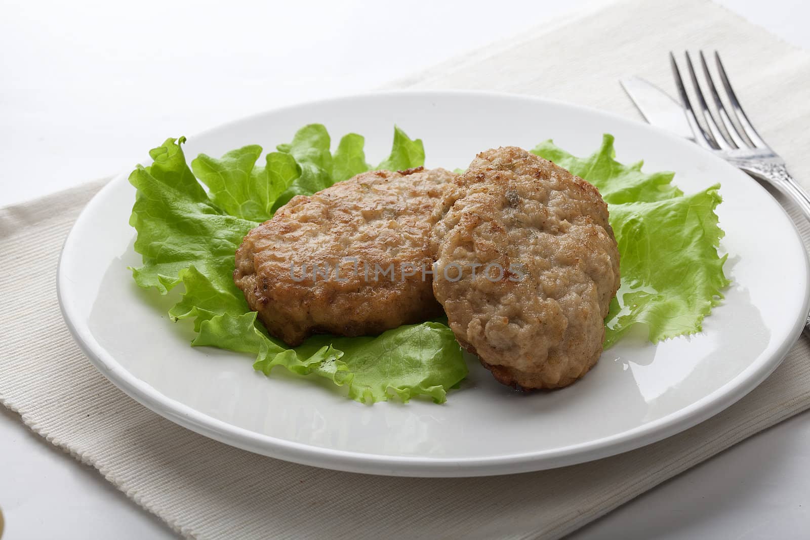 White plate with two rissoles and lettuce on the napkin with fork