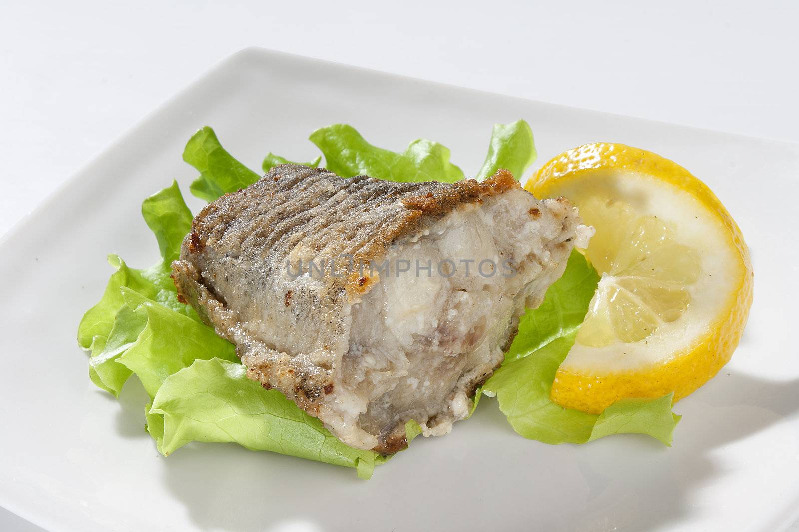 Fried piece of cod with lettuce and lemon on the plate