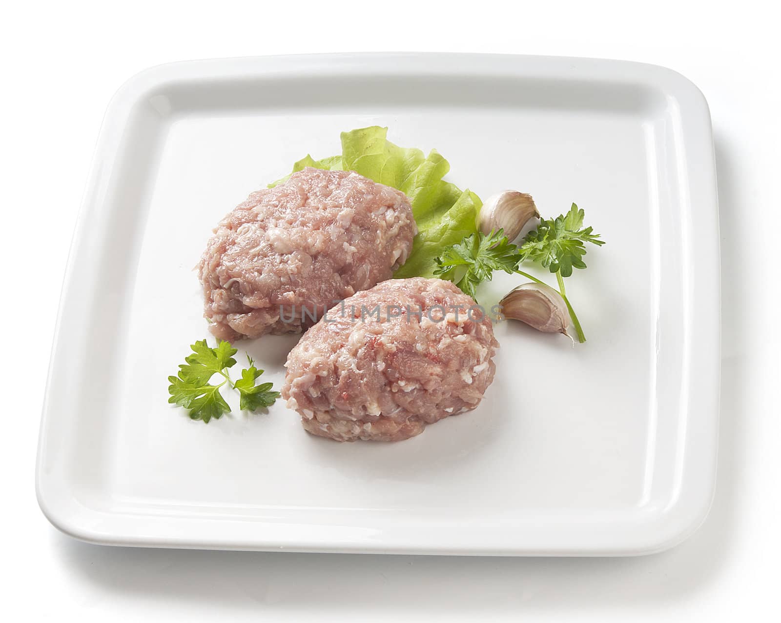 Two raw chicken rissoles with parsley, garlic and lettuce on the quad white plate