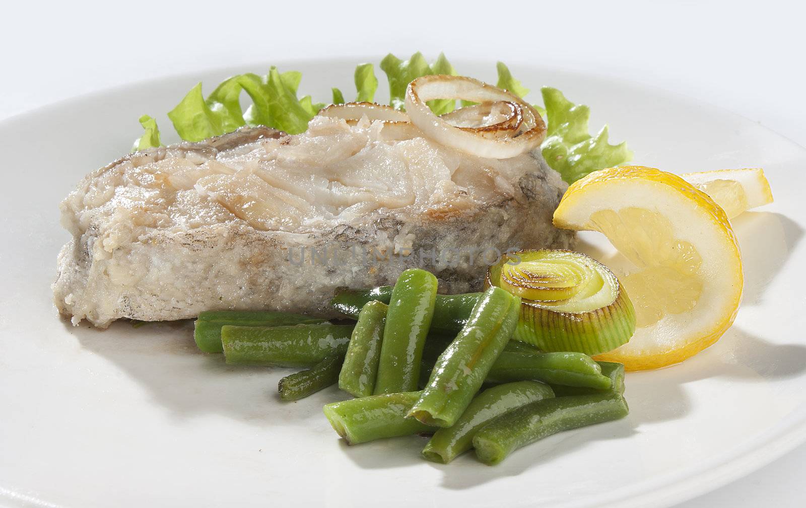 Fried piece of cod with lettuce, lemon, string beans and leek on the plate