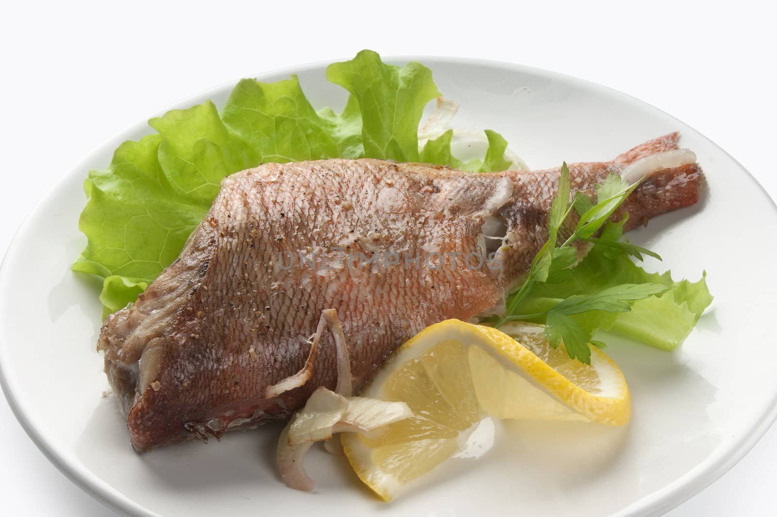 Baked rosefish with lettuce and lemon on the plate