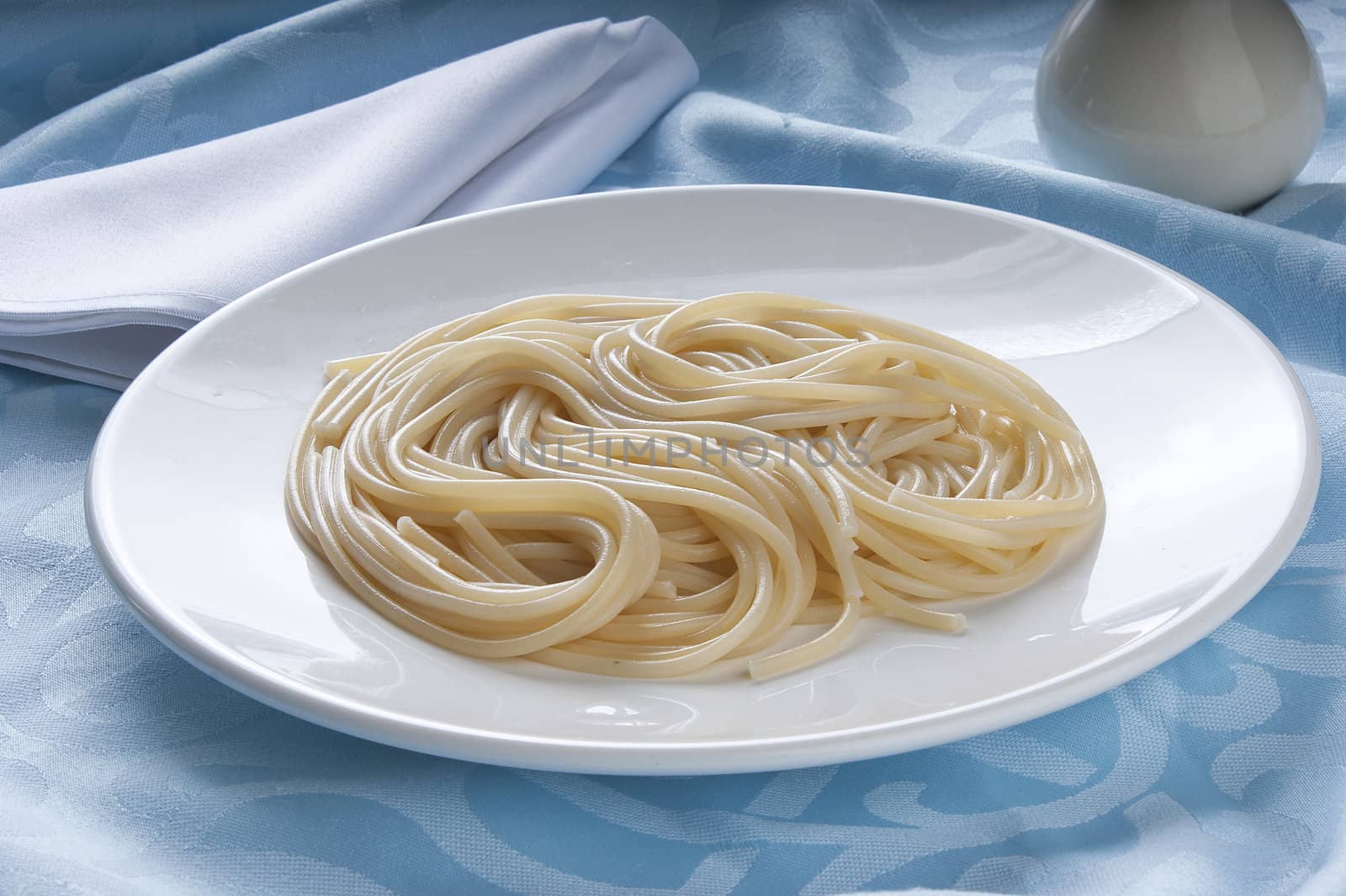 Plate with boiled spaghetti on the blue tablecloth