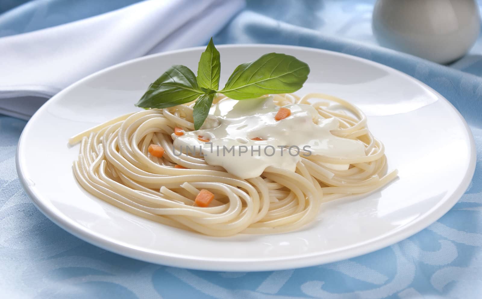 Spaghetti with cheese-cream sauce, carrot and basil on the white plate