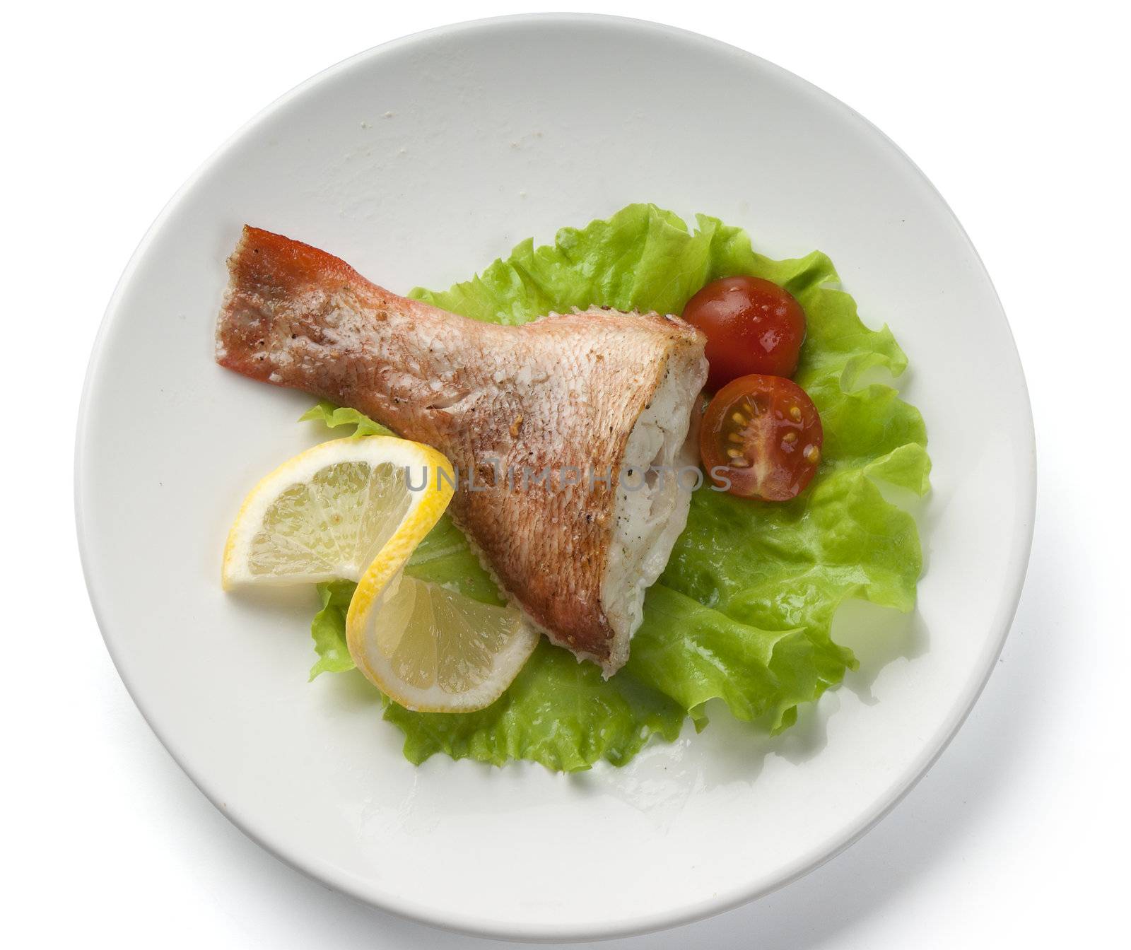 Baked rosefish with lettuce, tomato and lemon on the plate
