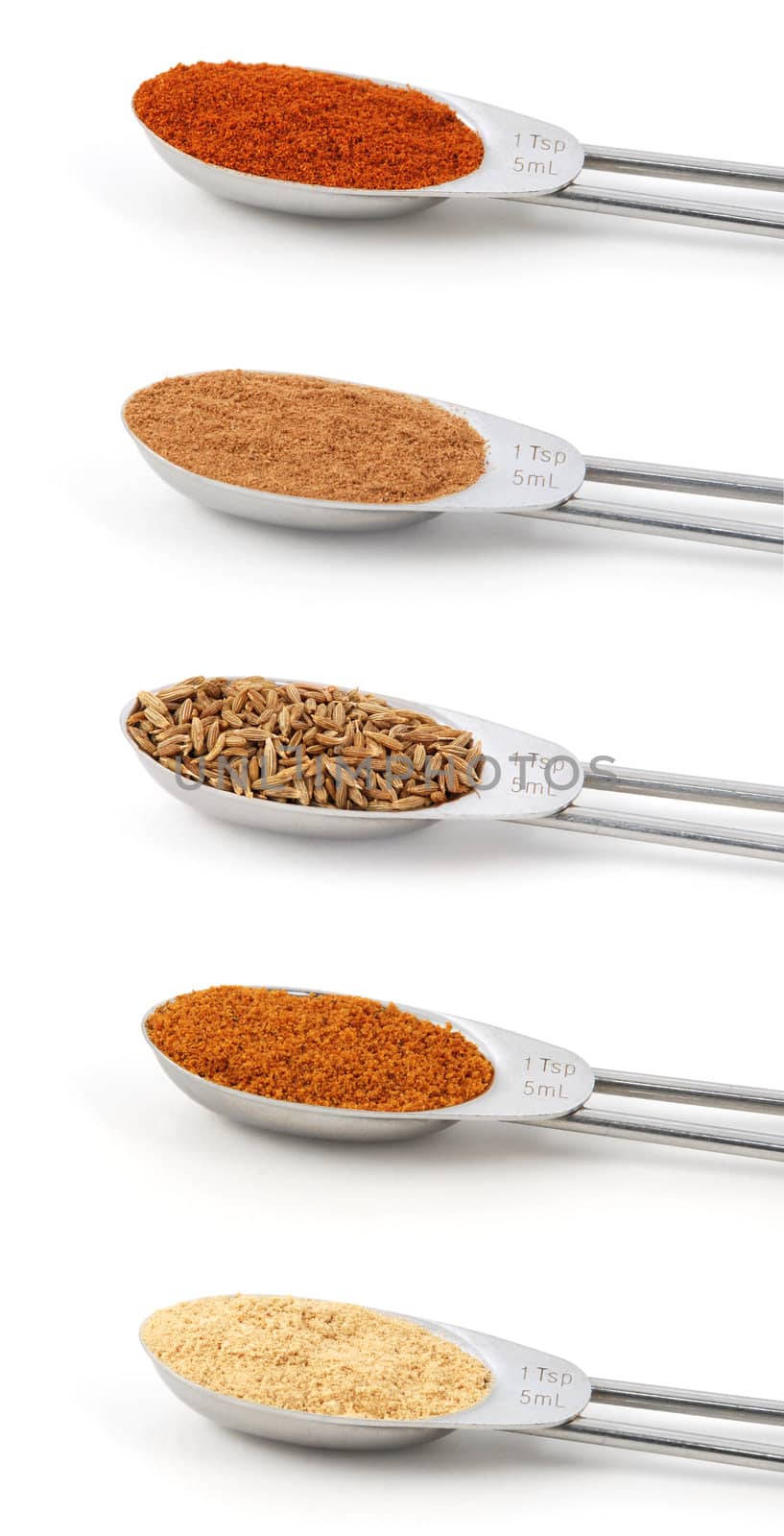 Spices measured in metal teaspoons, isolated on a white background: paprika, ground cinnamon, whole cumin seeds, ground mace and ground ginger.