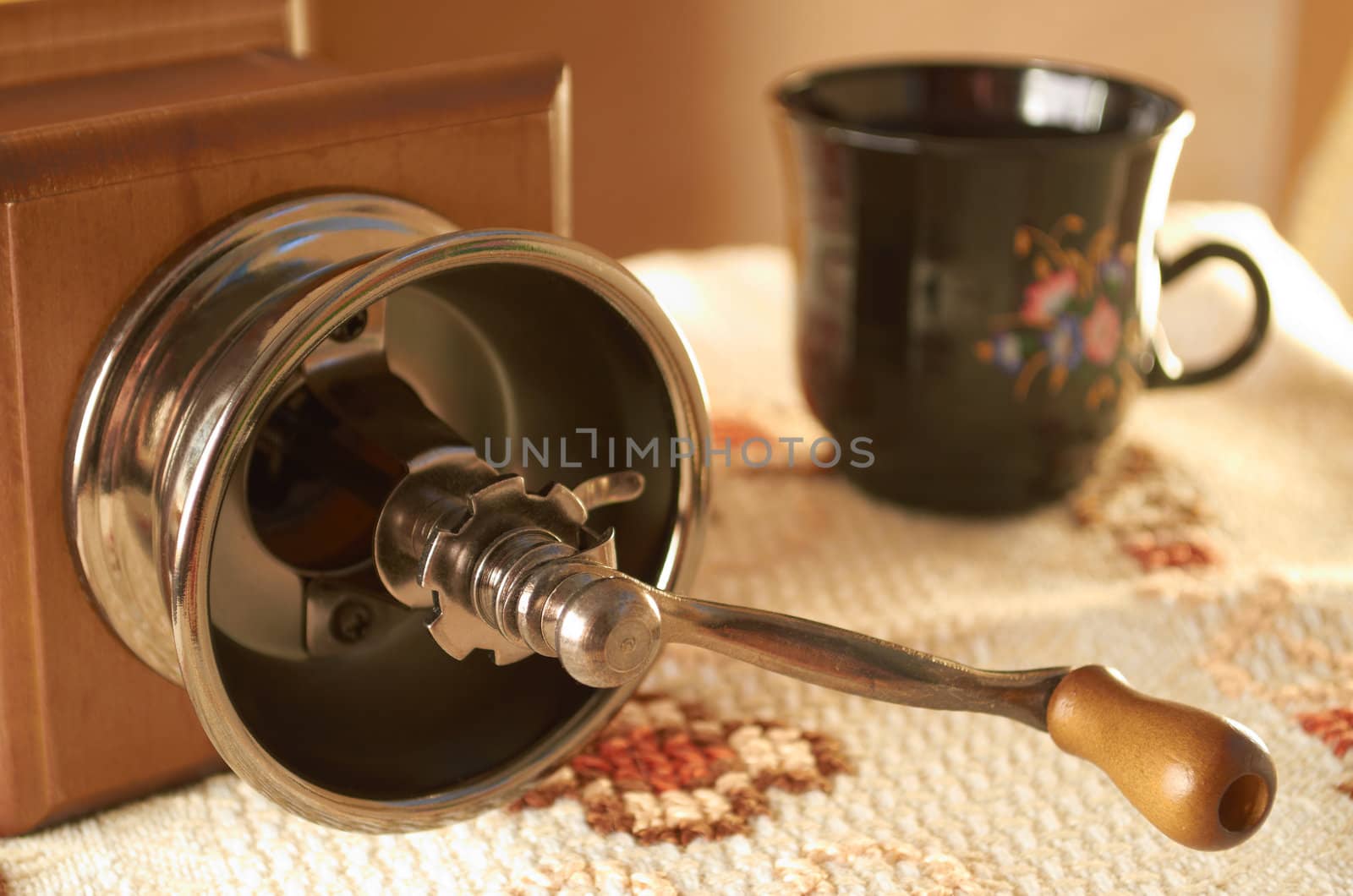Manual coffee grinder and ceramic cup on woven tablecloth