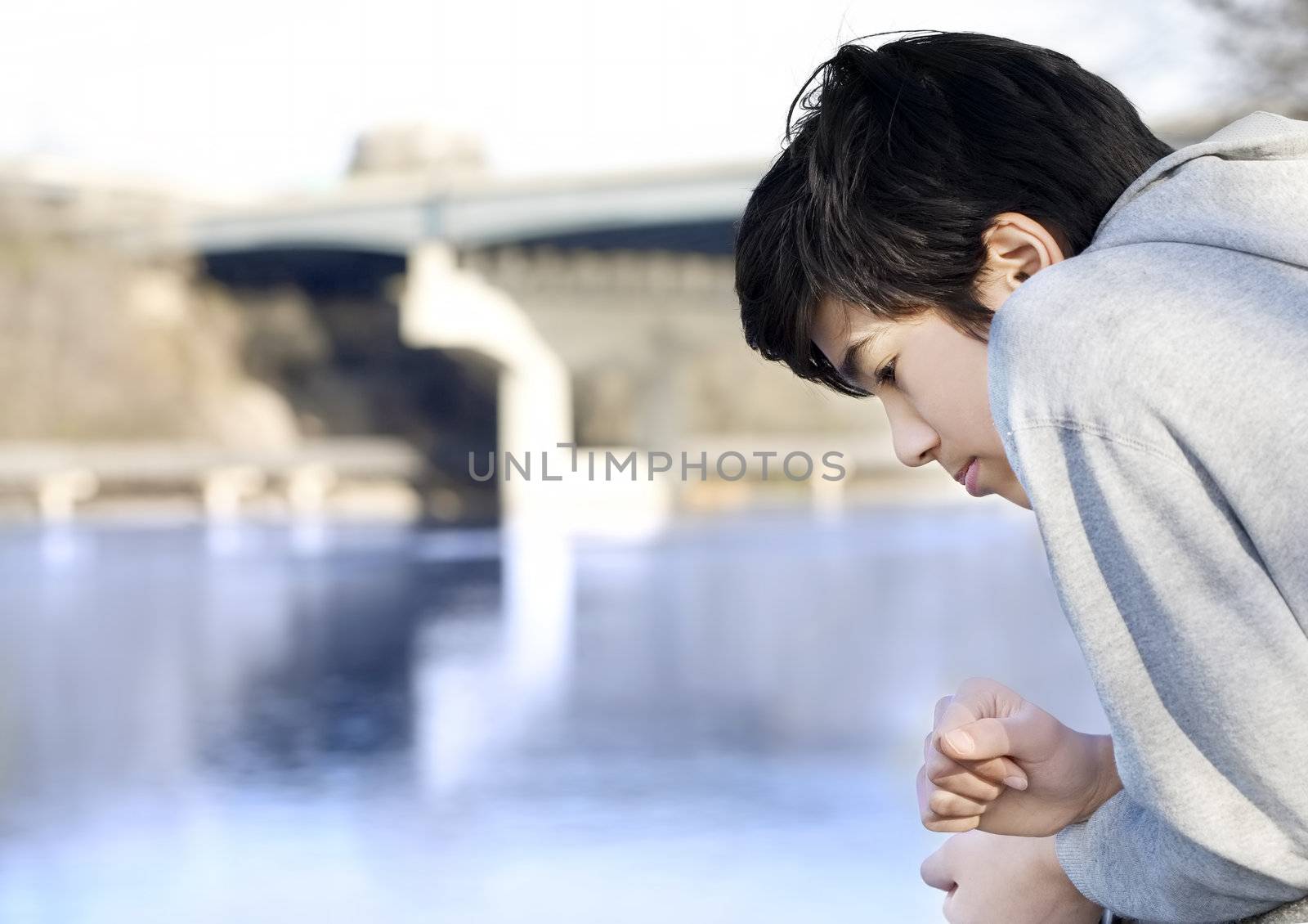 Teen boy sadly looking out over river, deep in thought