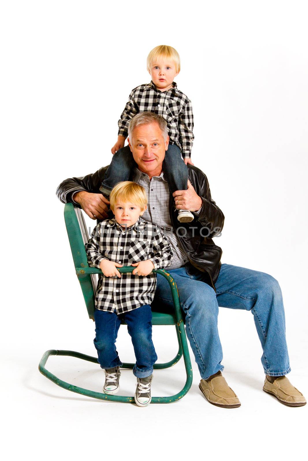 A grandfather with two boys in the studio on an isolated white background with a green rocking chair.