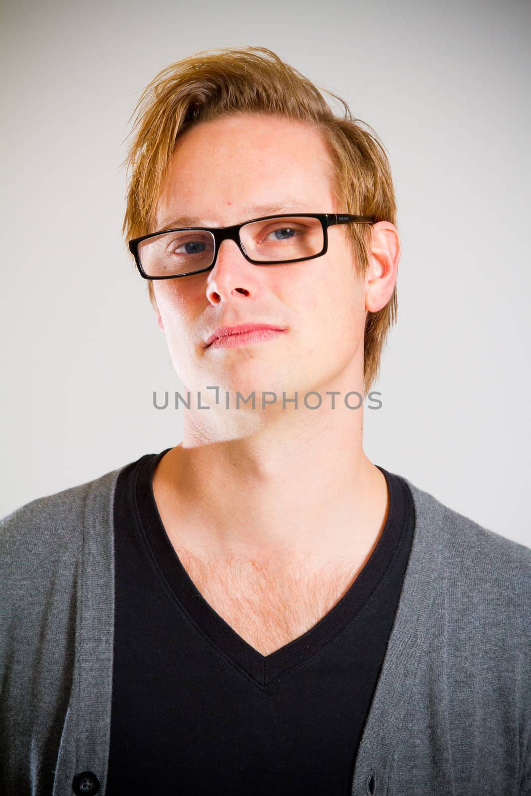 This contemporary style portrait of a man wearing a black shirt and a grey cardigan sweater while wearing glasses in the studio.