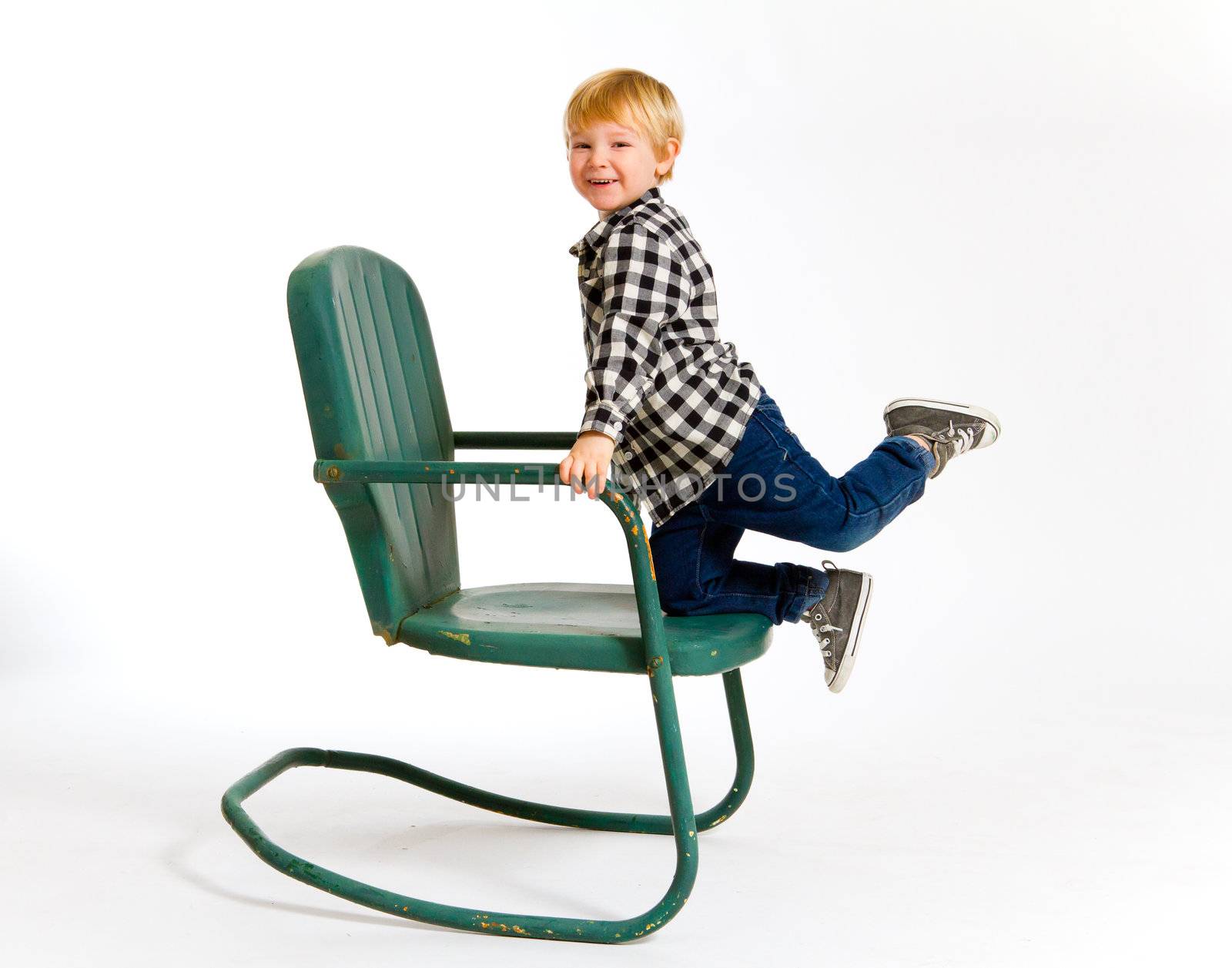 A boy in a plaid shirt has a fun time playing on this green rocking chair against an isolated white background in the studio.