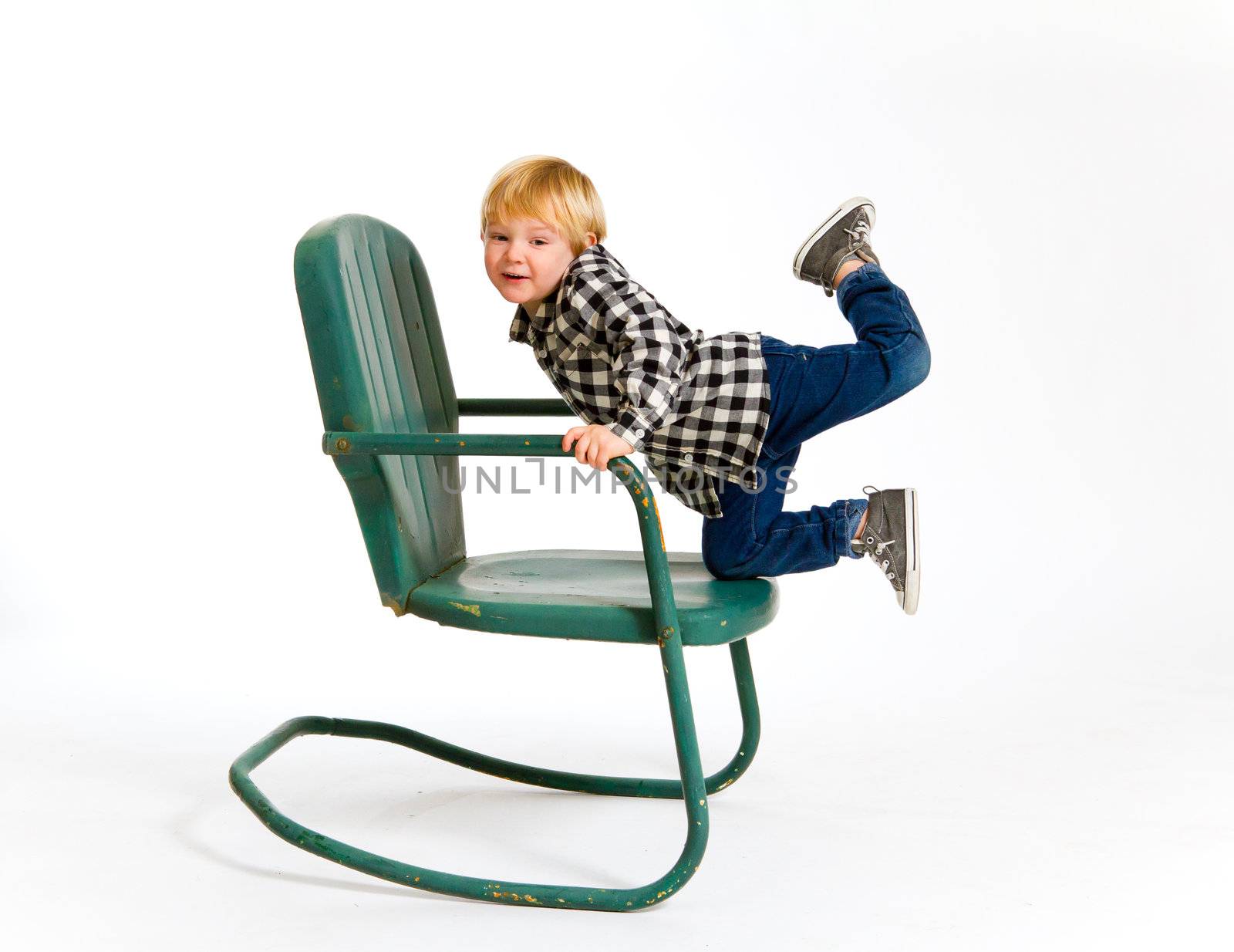 A boy in a plaid shirt has a fun time playing on this green rocking chair against an isolated white background in the studio.