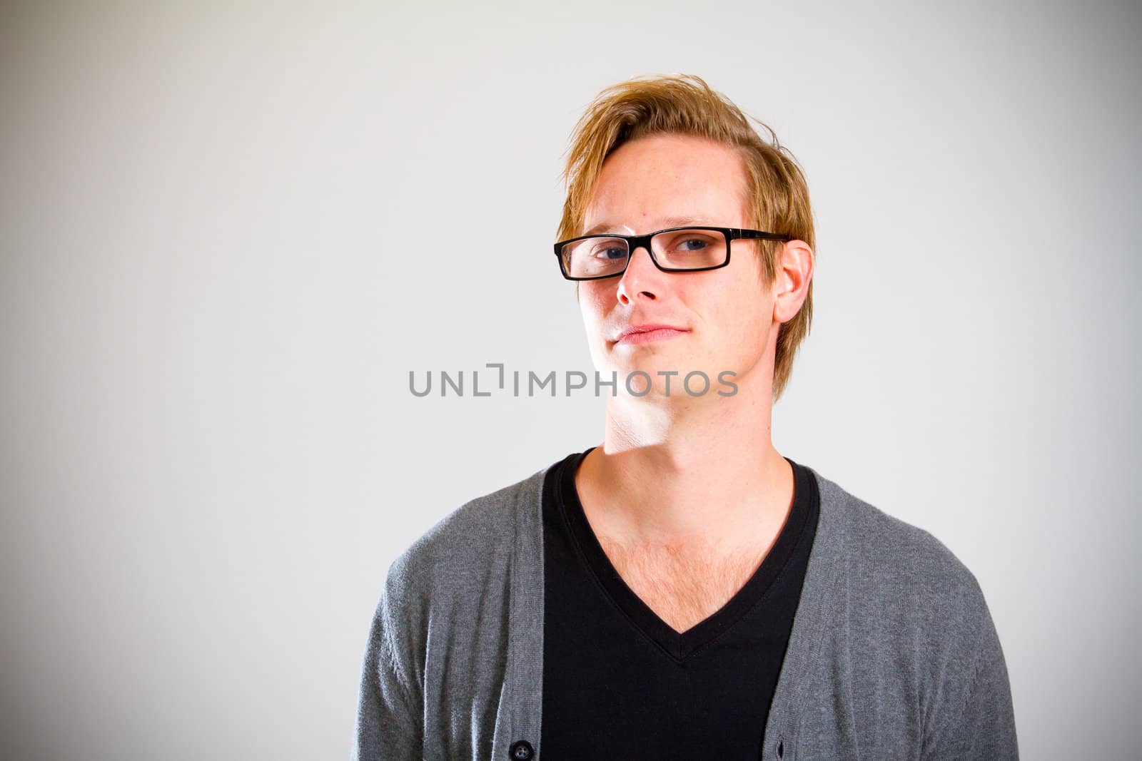 This contemporary style portrait of a man wearing a black shirt and a grey cardigan sweater while wearing glasses in the studio.