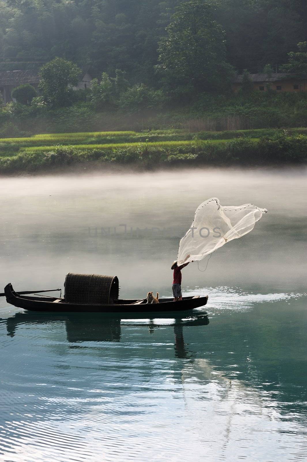 A fisherman casting his net from the boat on the river