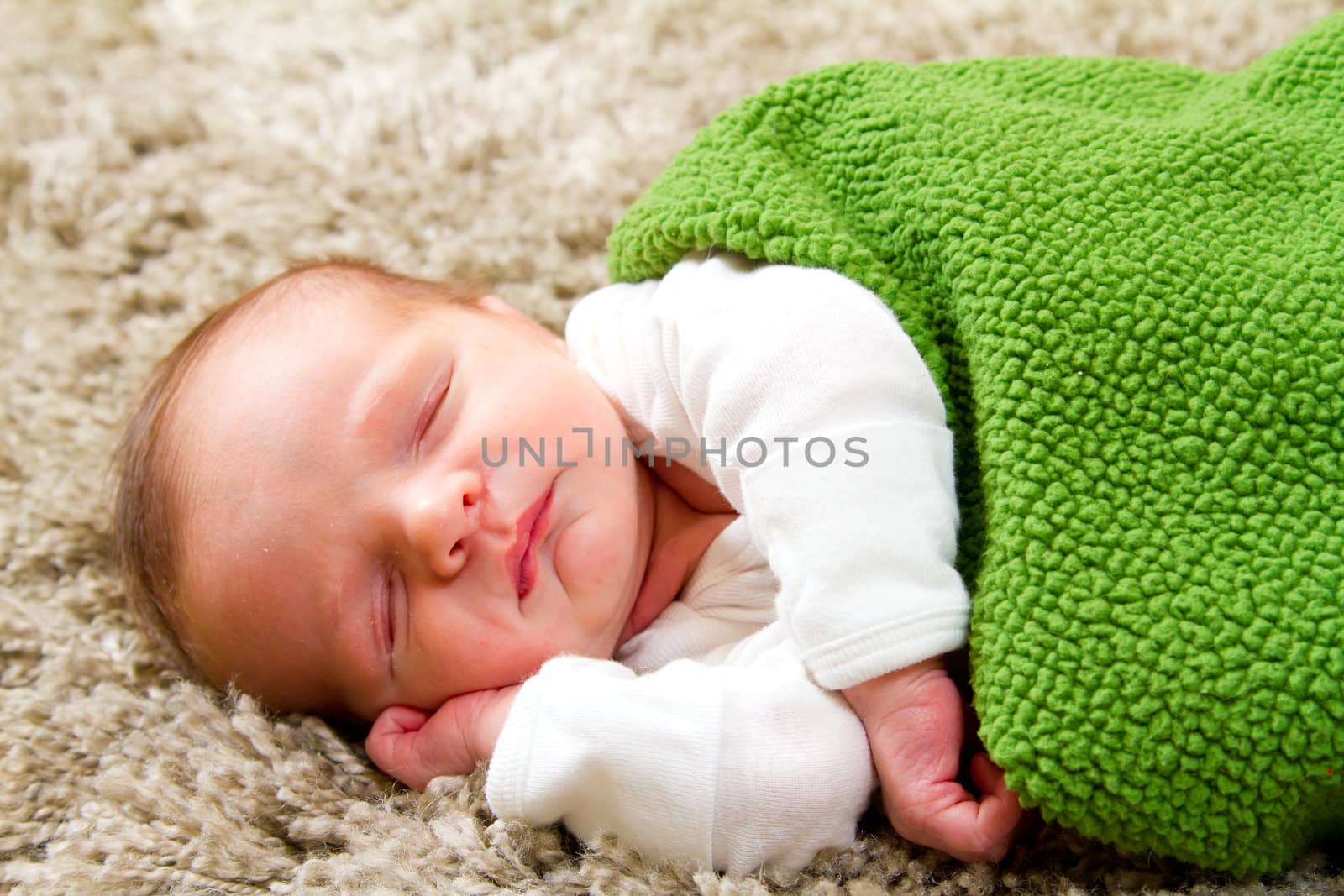 A young newborn baby boy rests wrapped up in a blanket and looking comfortable and cozy.