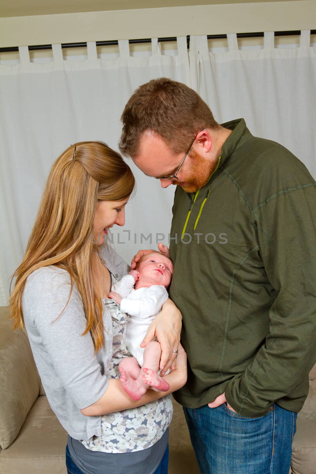A mother and father hold their newborn baby son in their arms and look towards him showing happiness and caring emotions.