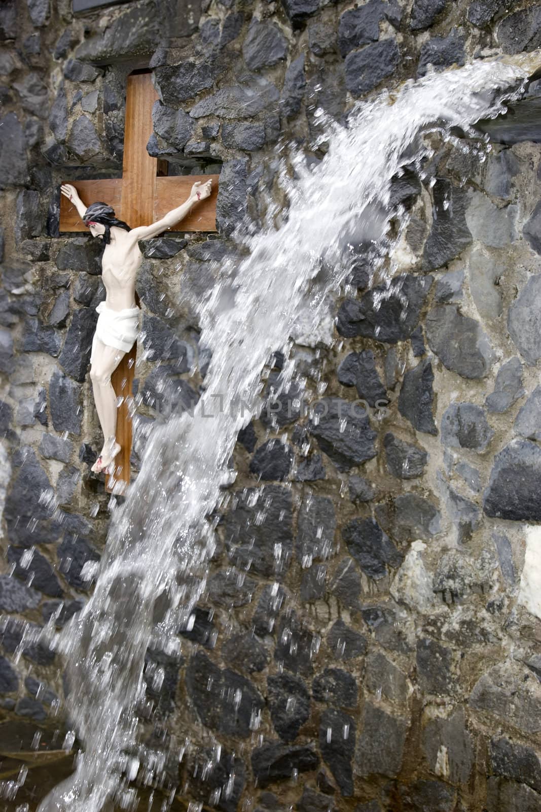 crusifix of jesus on wood cross embedded in rocks with a waterfall in the foreground