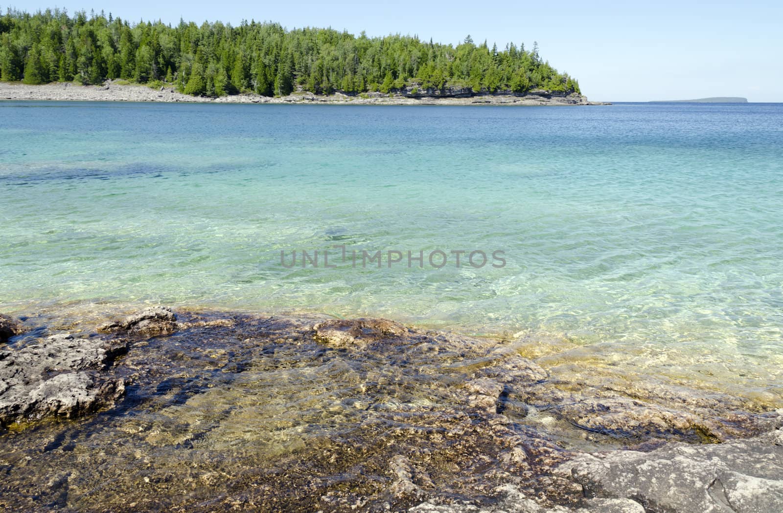 Green and blue water of Huron Lake, Ontario under blue sky.