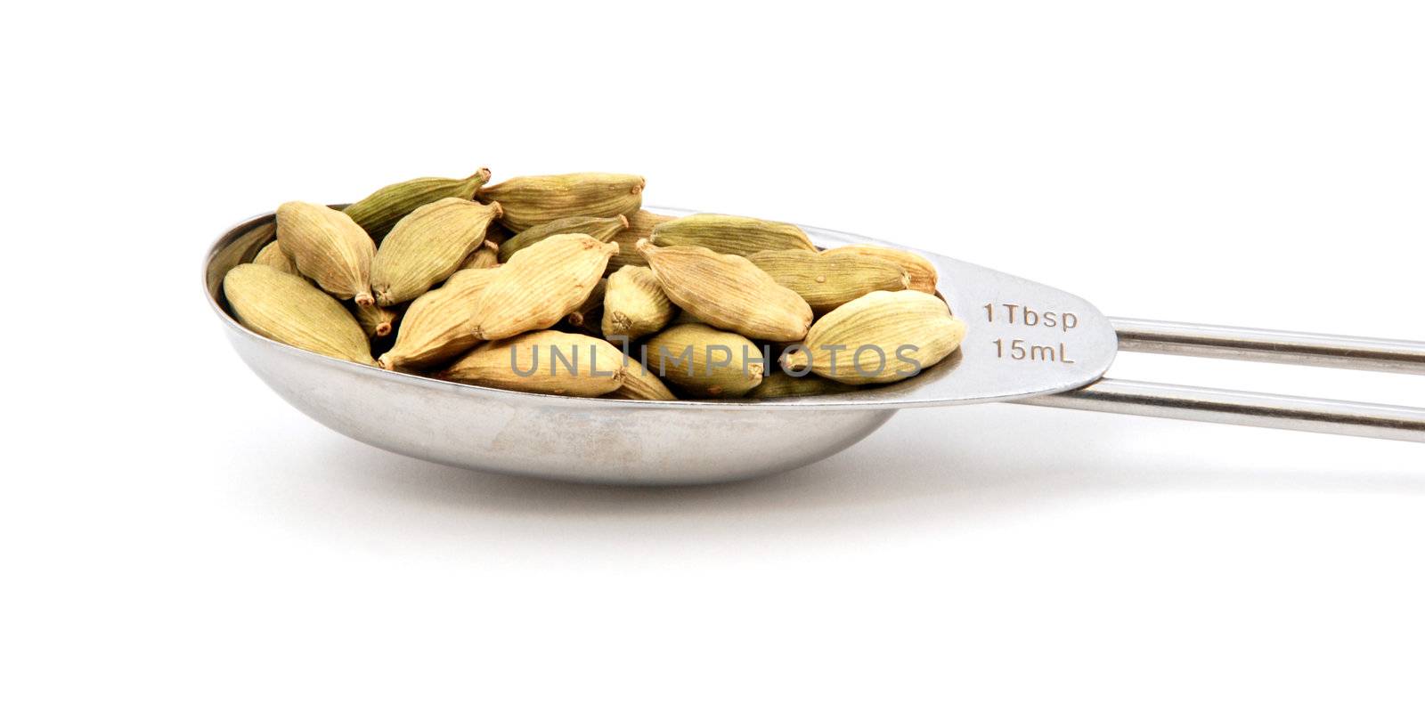 Cardamom pods measured in a metal tablespoon, isolated on a white background