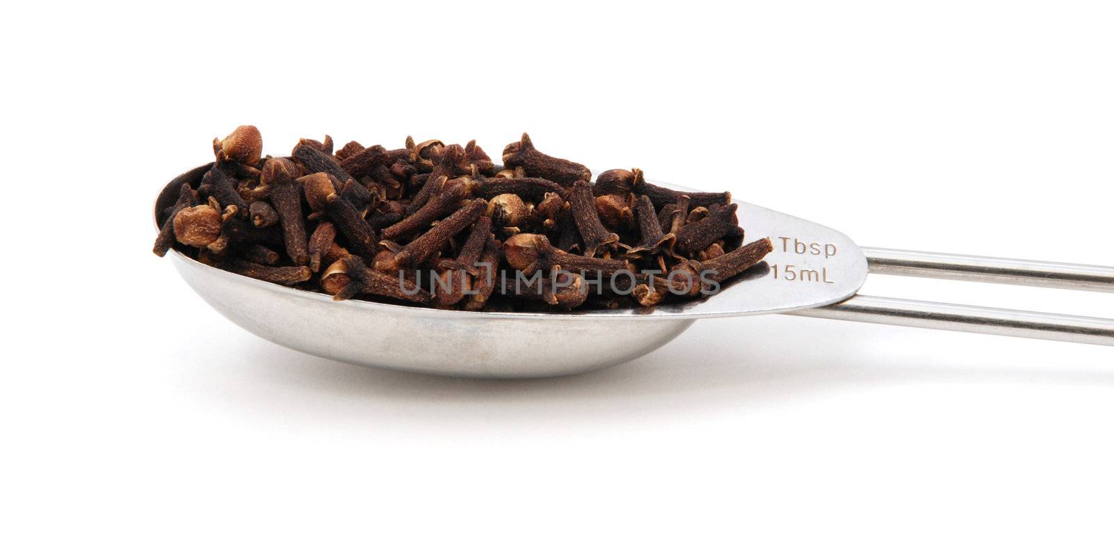 Whole cloves measured in a metal tablespoon, isolated on a white background