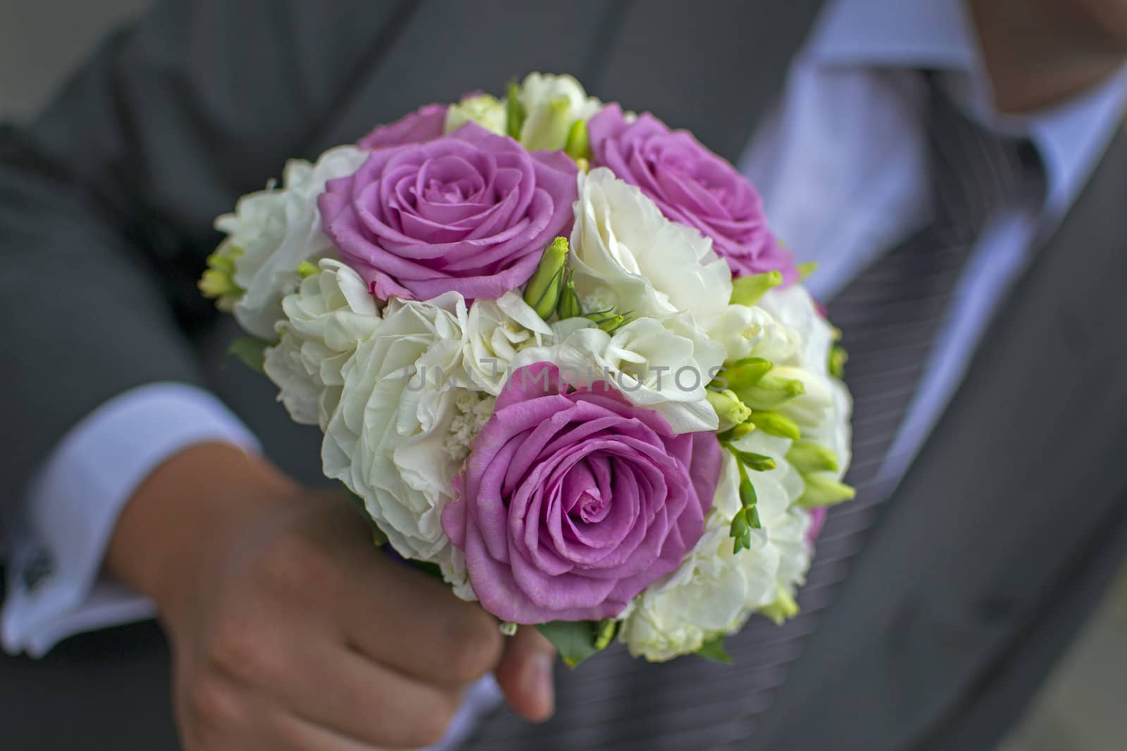 An elegant hand-tied bouquet or bunch of flowers in the hand of a groom or man.