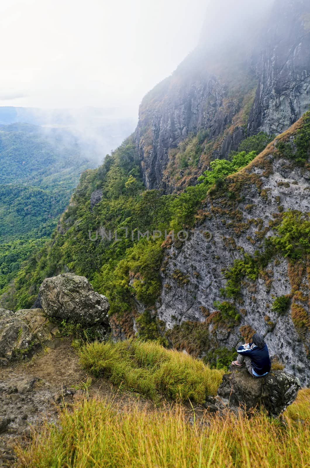 Young man in foggy mountain sitting on a rock by the cliff