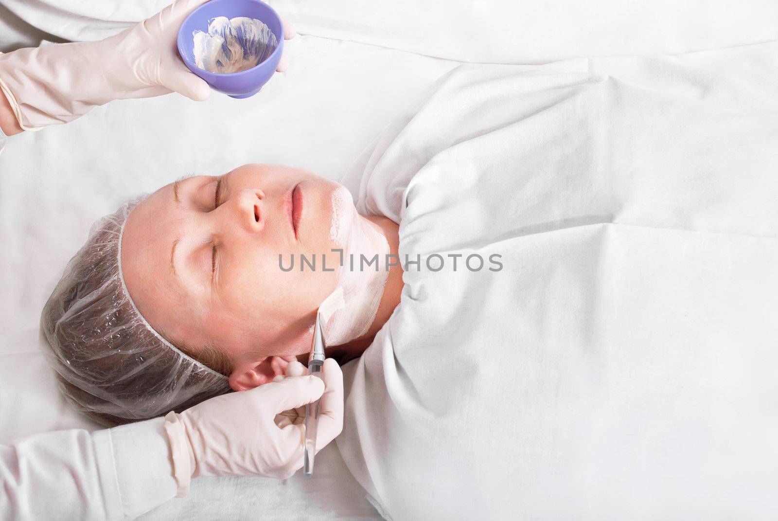 Woman on the procedure in the beauty salon, applying a facial mask.