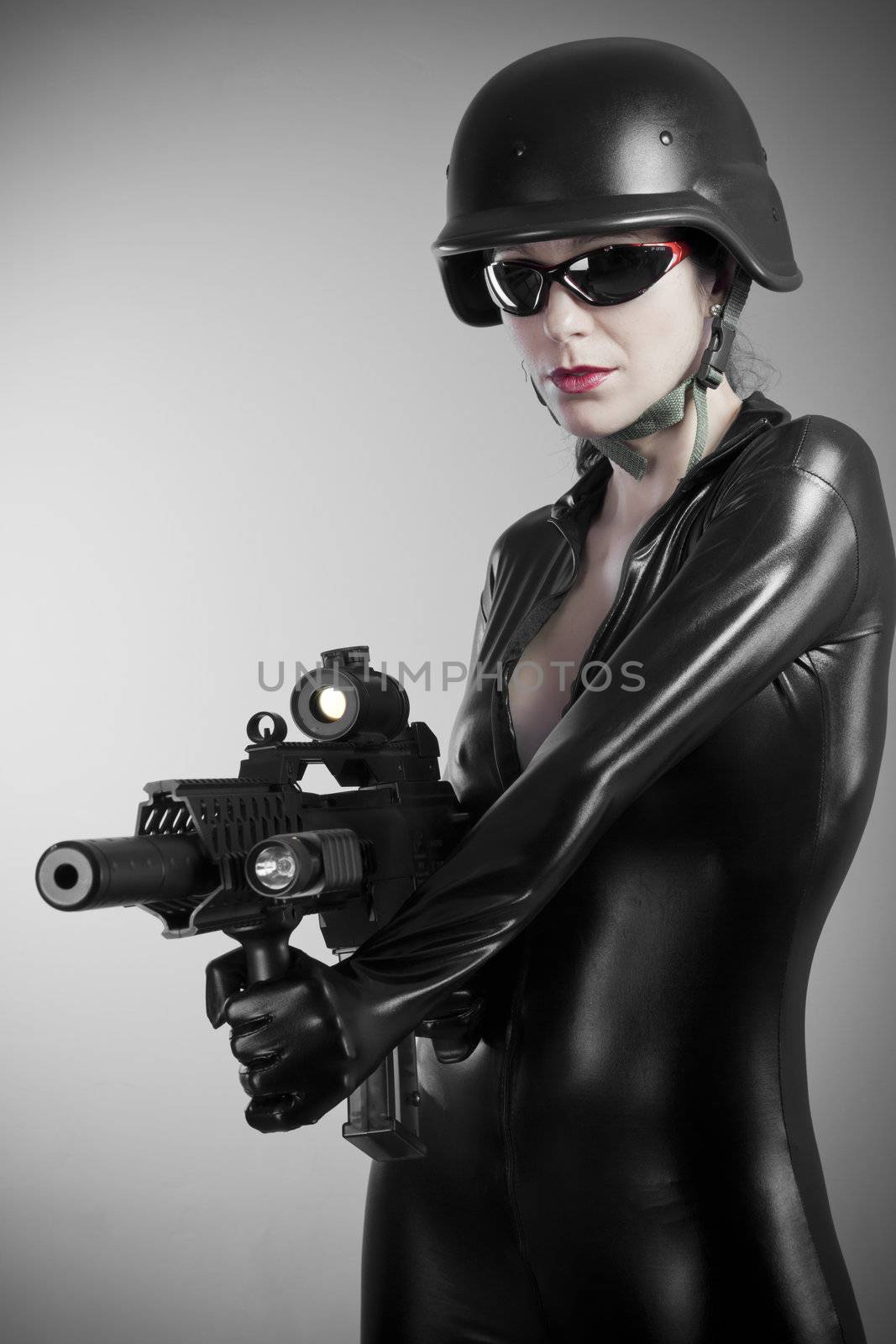 Sexy brunette woman in latex jumpsuit with heavy gun and helmet