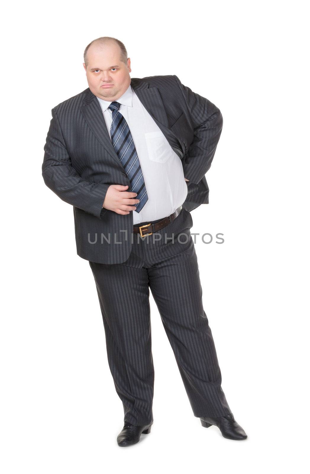 Fat overweight businessman in a stylish suit standing with his hand on his hip glowering at the camera with a displeased expression, studio portrait on white