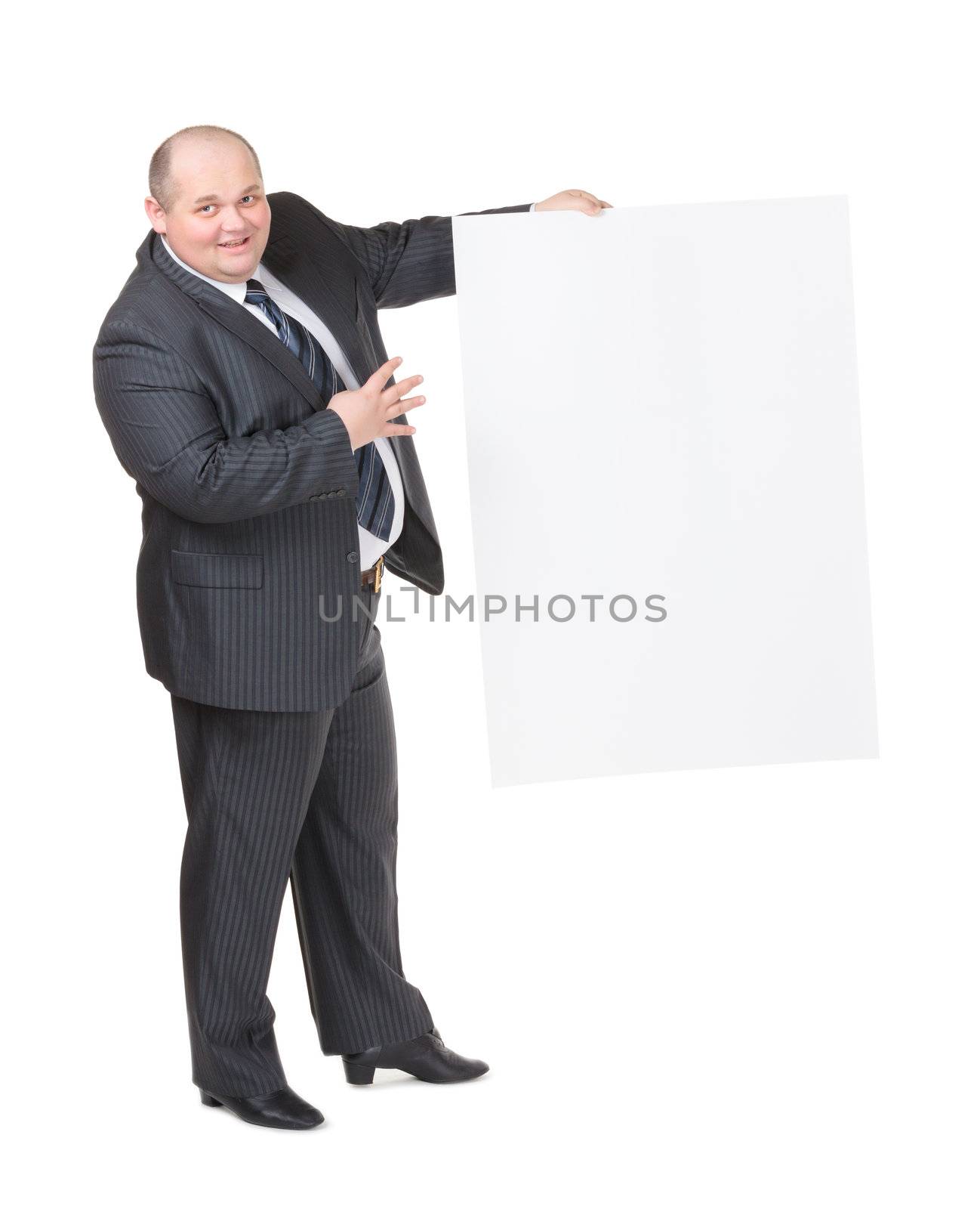 Cheerful overweight stylish business man in a suit holding up a blank white sign and pointing to it with his finger on a white studio background