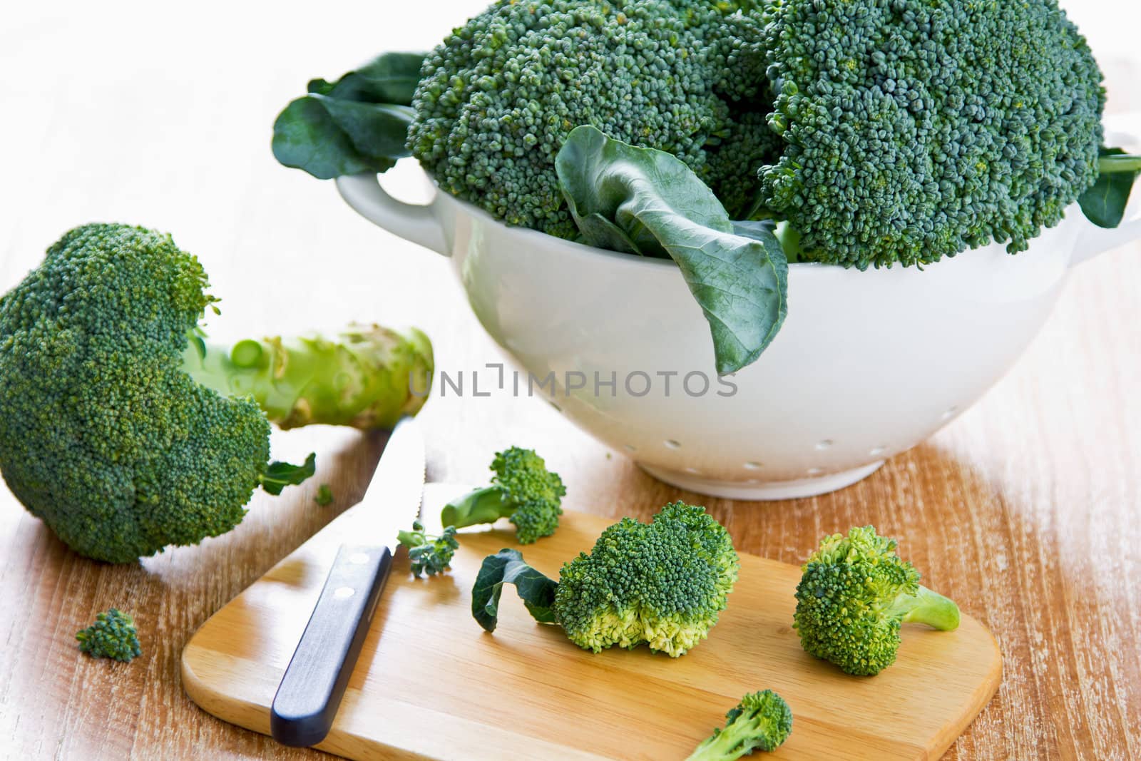 Fresh uncooked broccoli in colander and chopping board