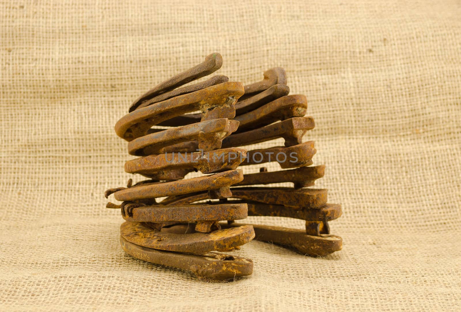 heap of old retro rusty horseshoes on burlap material background.