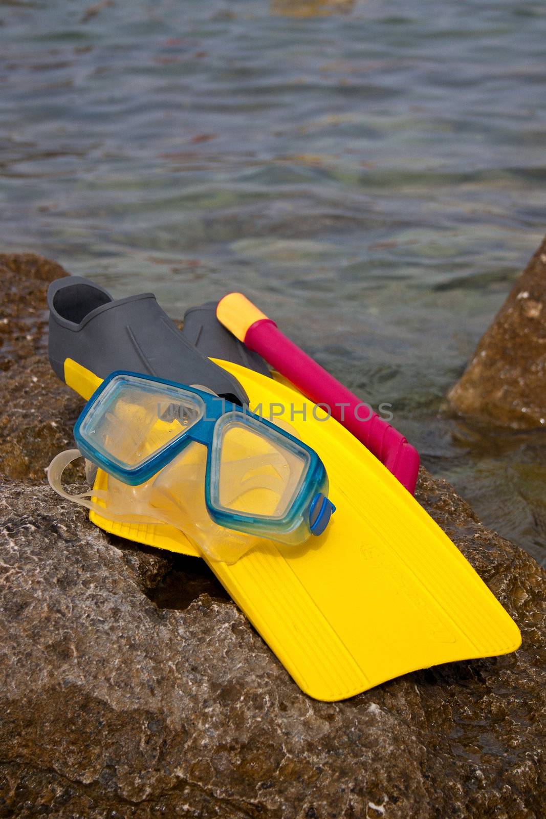 Yellow flippers with snorkel goggle and tube on a rock near the sea