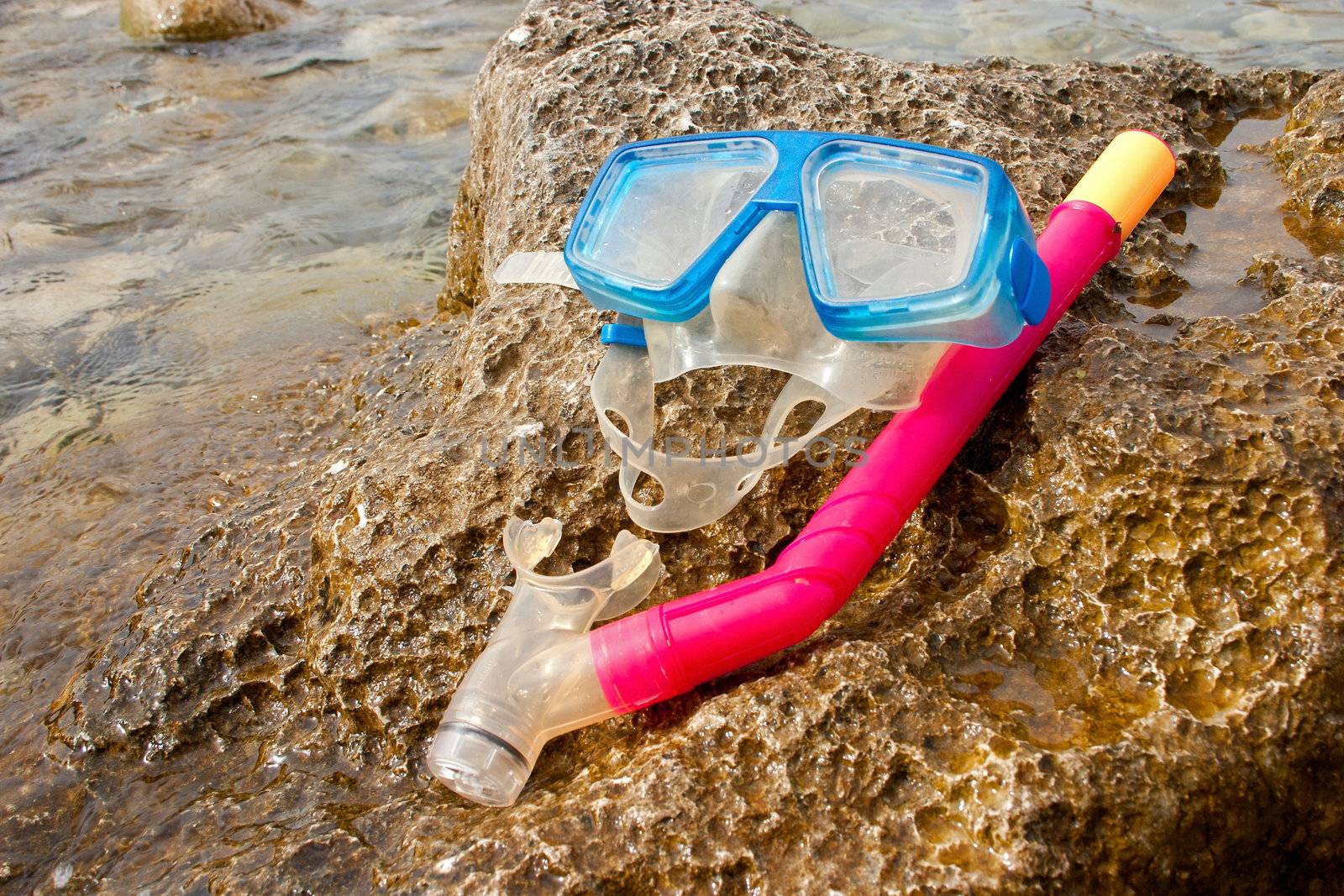 Blue snorkel goggle and tube on a rock near the sea