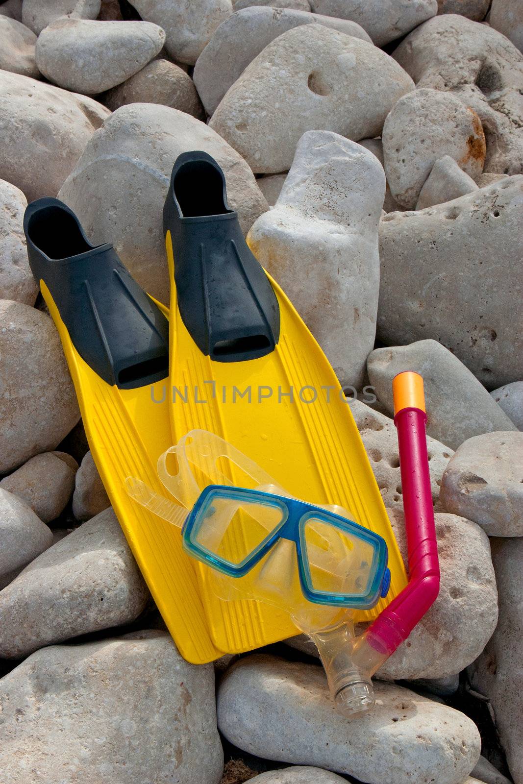 Yellow flippers with snorkel goggle and tube on a rock near the sea