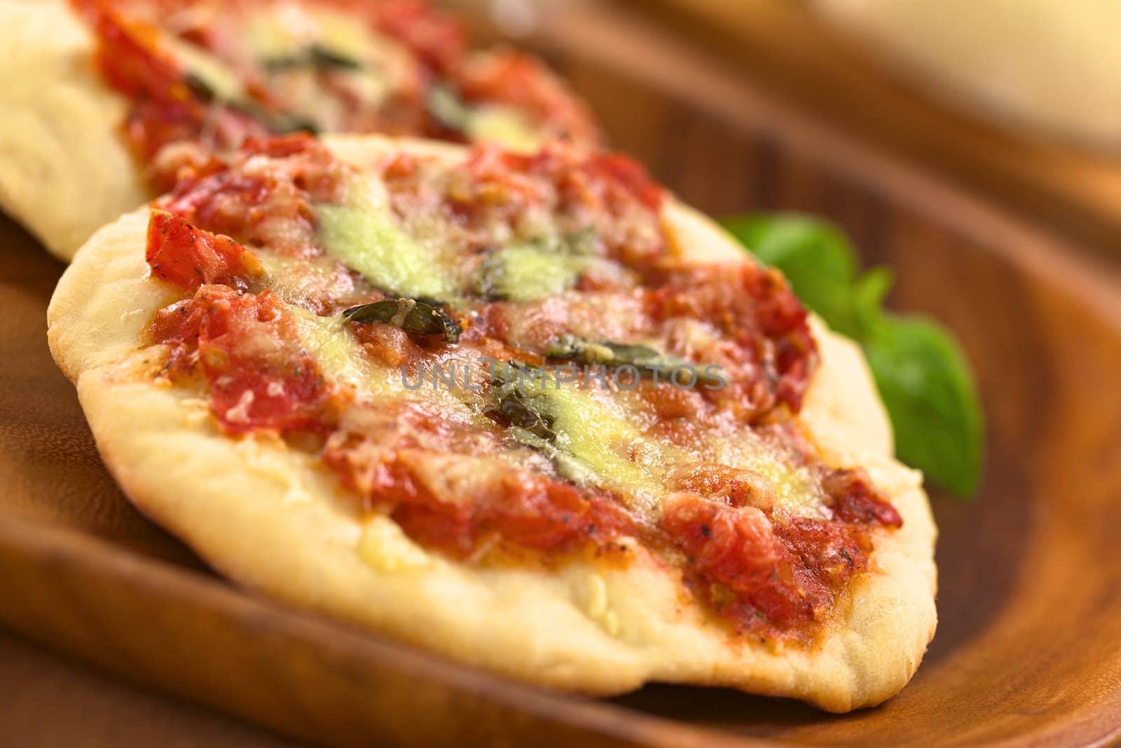 Crispy homemade Pizza Margherita or Pizza Mozzarella (pizza with tomato, basil and cheese) on wooden plate (Selective Focus, Focus one third into the first pizza)