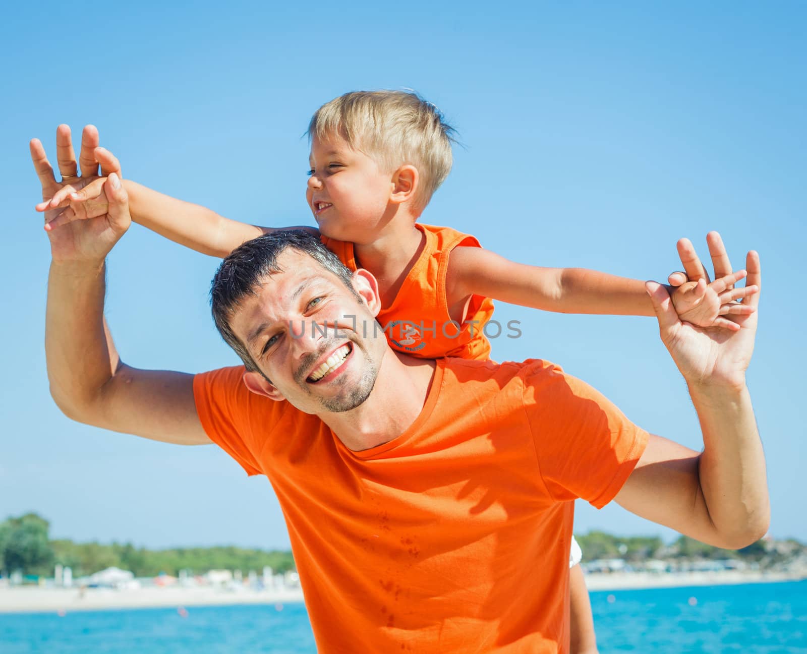 Clouseup portrait of happy father with son laughing and looking at camera on the beach