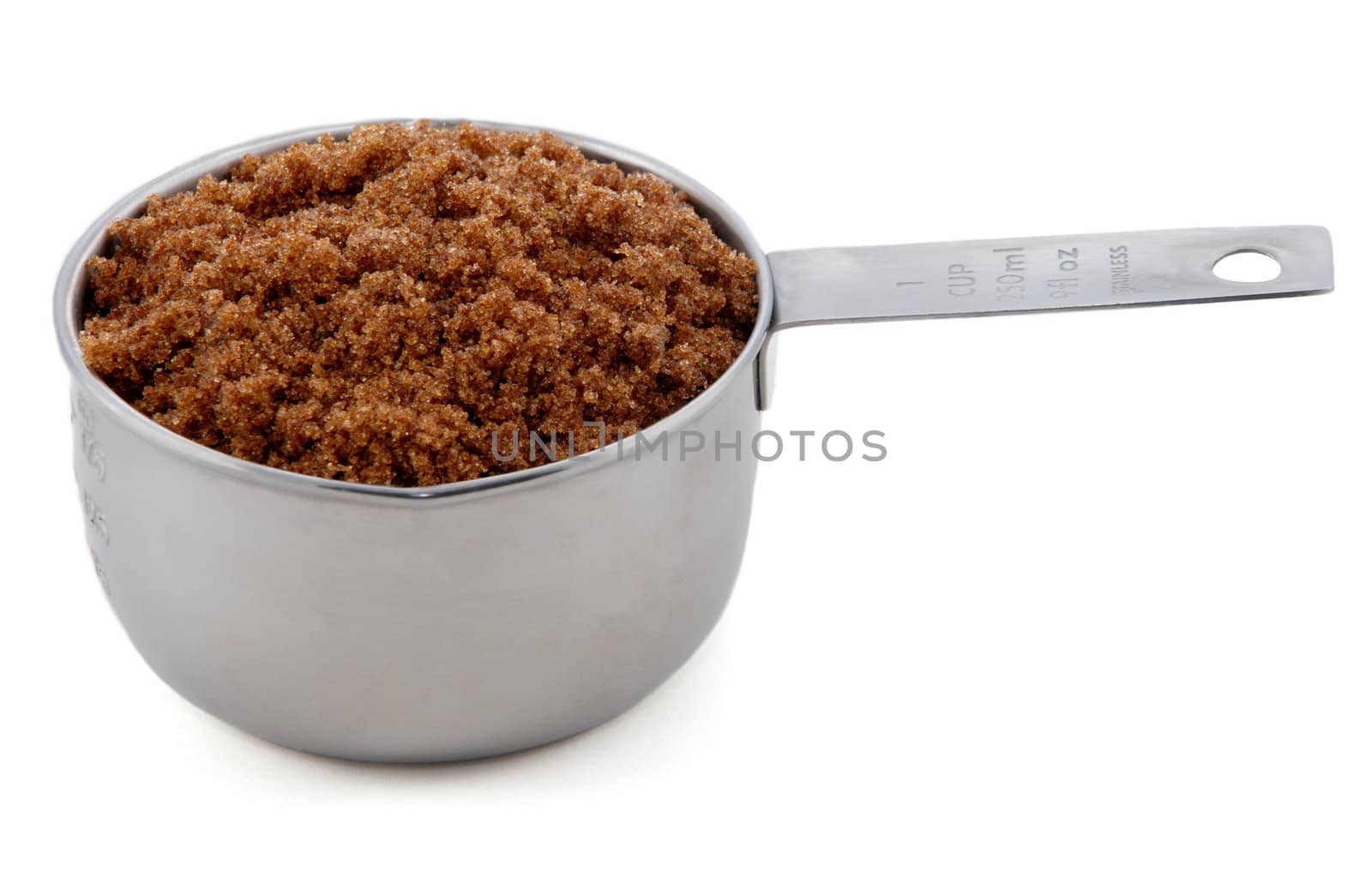 Dark brown soft / muscovado sugar presented in an American metal cup measure, isolated on a white background