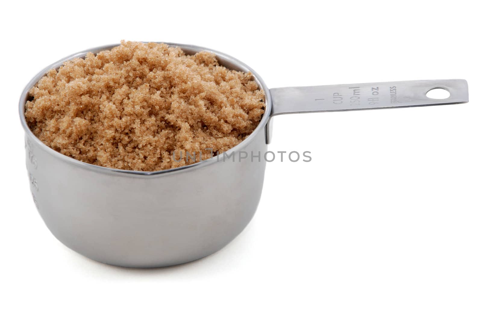 Light brown soft / muscovado sugar presented in an American metal cup measure, isolated on a white background